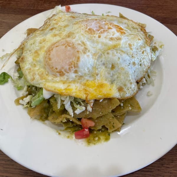 Chilaquiles with green sauce, topped with two fried eggs, crumbled cheese, and diced tomatoes.