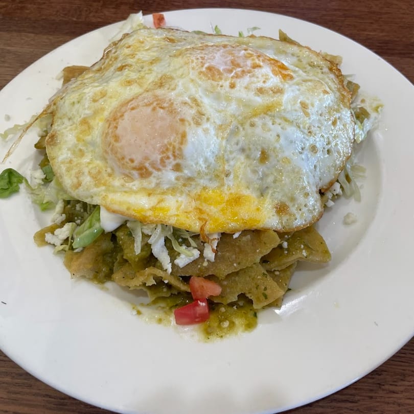 Chilaquiles with green sauce, topped with two fried eggs, crumbled cheese, and diced tomatoes.