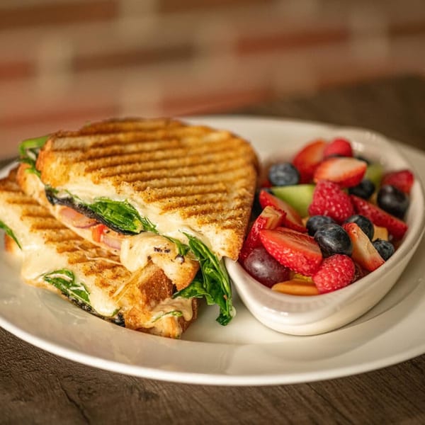 Grilled panini sandwich with melted cheese and spinach, served with a side of fresh fruit salad.