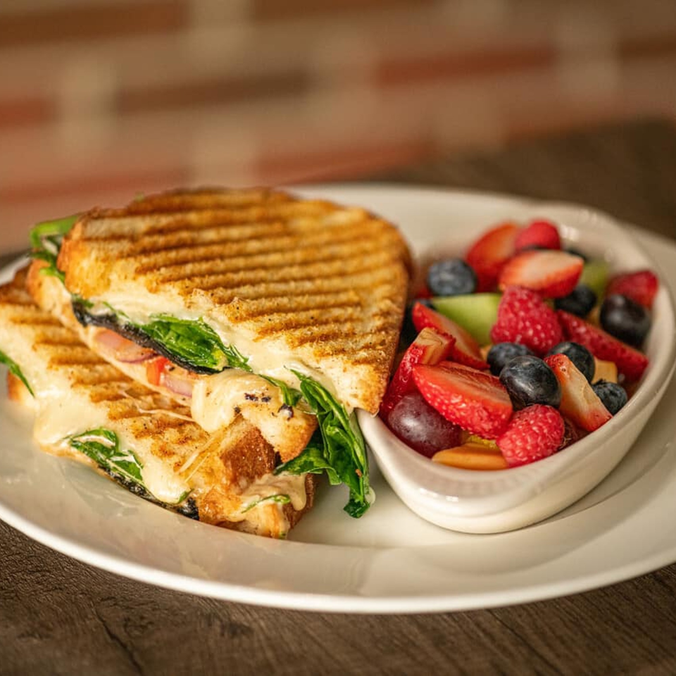Grilled panini sandwich with melted cheese and spinach, served with a side of fresh fruit salad.