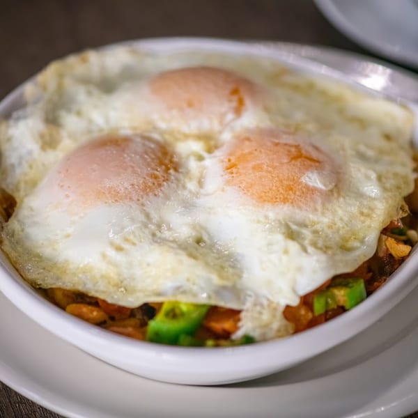 Three fried eggs with bright orange yolks and white whites, served over a breakfast hash.