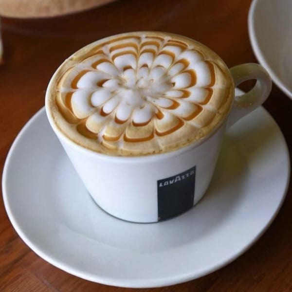 A white Lavazza cup filled with a cappuccino, featuring intricate caramel latte art on top.