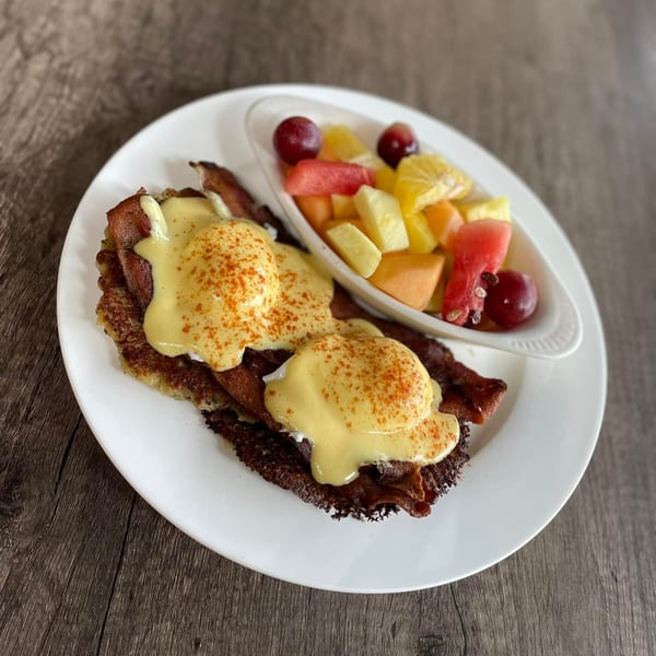 Eggs Benedict with bacon and hash browns, served with a side of fresh fruit.