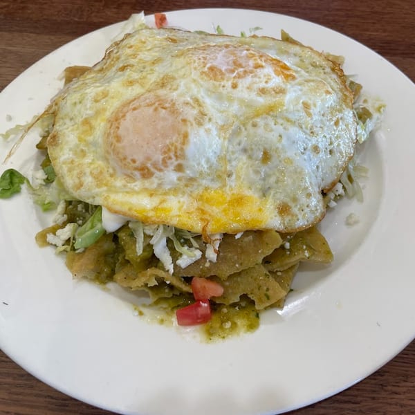 Chilaquiles with green sauce, topped with two fried eggs, crumbled cheese, and diced tomatoes.