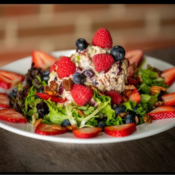 Chicken salad with raspberries, blueberries, strawberries, and pecans on a bed of mixed greens.