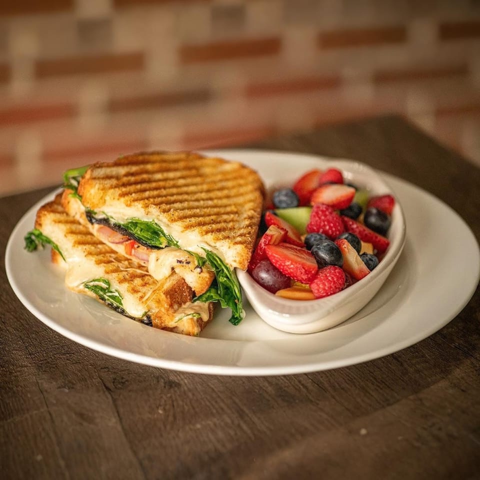 Grilled panini sandwich with melted cheese and spinach, served with a side of fresh mixed berries.