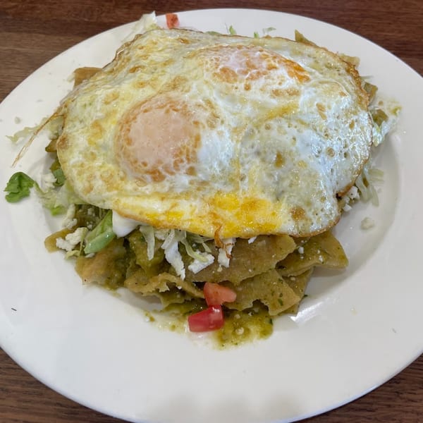 Chilaquiles with green sauce, topped with two fried eggs, lettuce, cheese, and diced tomatoes.