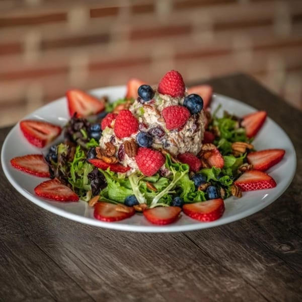 Chicken salad with raspberries, blueberries, strawberries, and pecans on a bed of greens.