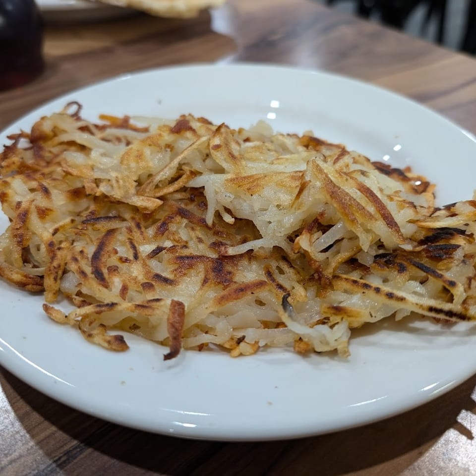 Golden brown, crispy hash browns on a white plate, ready to be enjoyed for breakfast.