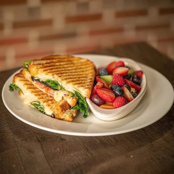 Grilled panini sandwich with melted cheese and spinach, served with a side of fresh fruit salad.