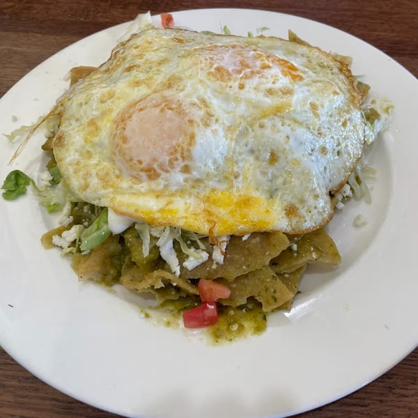 Chilaquiles with green sauce, topped with two fried eggs, lettuce, cheese, and diced tomatoes.