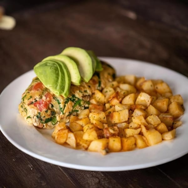 Garden Berry Cafe's omelet with avocado slices and a side of seasoned breakfast potatoes on a white plate.